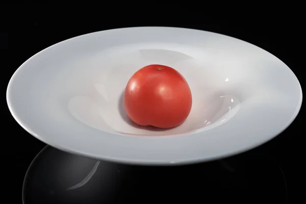 Una verdura de tomate en un plato blanco, sobre un fondo negro — Foto de Stock