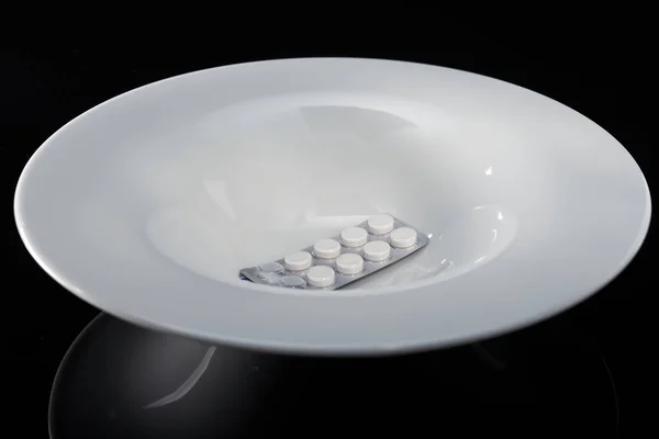 Pílulas medicinais em uma placa branca em um fundo preto . — Fotografia de Stock