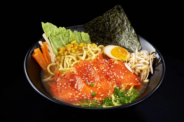 Asian ramen soup with salmon steaks in a black plate, on a black background — Stock Photo, Image
