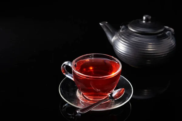 Coupe en verre avec thé rouge chaud et théière sur un fond noir . — Photo