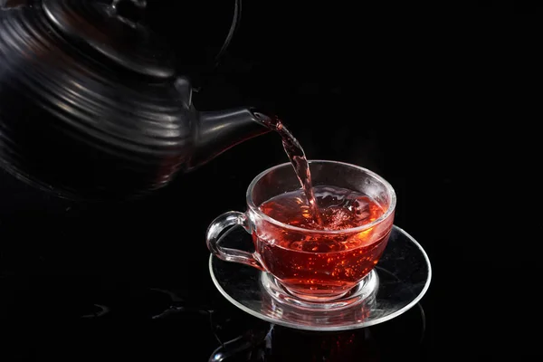 紅茶を急須から黒の背景にグラスカップに注ぎます。 — ストック写真