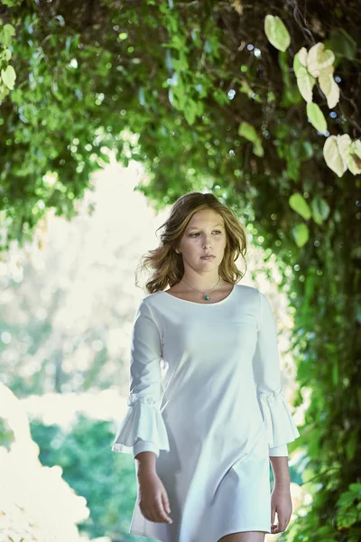 Schöne Teenager-Mädchen mit langen Haaren in einem weißen kurzen Kleid. ein Mädchen spaziert im Park. — Stockfoto