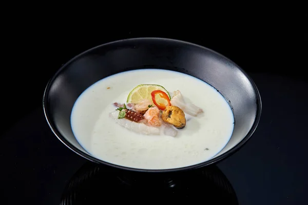 Балийский сливочный суп с морепродуктами в черной тарелке на темной спине — стоковое фото
