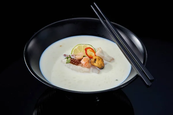 Балийский сливочный суп с морепродуктами в черной тарелке на темном фоне — стоковое фото