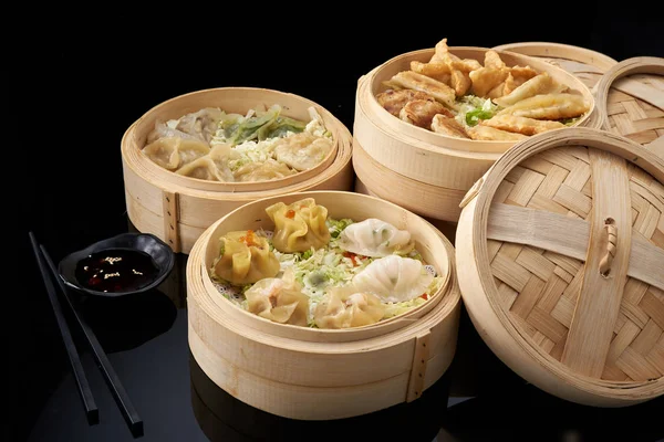 Aziatische keuken: een set knoedels in bamboe dubbele boiler op een donkere achtergrond — Stockfoto