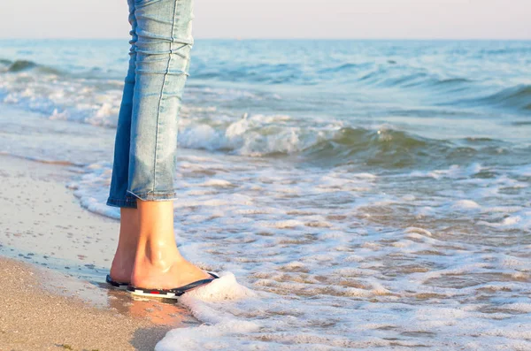 legs of a girl in jeans and sandals in a sea wave, a horigont of the sky