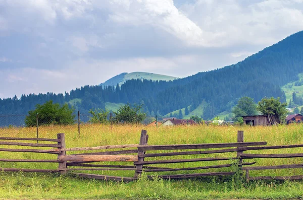 wooden fence in a meadow in the mountains, houses in the background