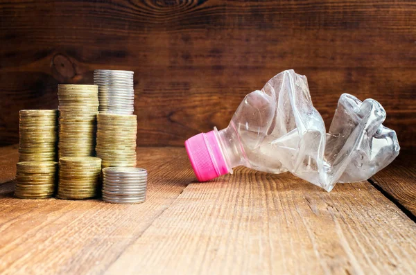 Stapel Von Münzen Eine Weggeworfene Plastikflasche Auf Einem Hölzernen Hintergrund lizenzfreie Stockbilder