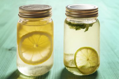 iki cam kavanozların kapakları güneş tarafından aydınlatılmış bir turkuaz ahşap tablo ile bir limon ve limon ve nane ile diğer soğuk suyla vardır