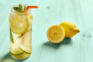 limon limonata bir cam kavanoza yanında turkuaz ahşap bir masa üzerinde sürahi su, dilim limon ve kireç, buz, nane yaprakları ve bir baston içecek içerir
