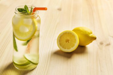 limon limonata bir cam kavanoza yanındaki ahşap bir masa üzerinde su, limon ve kireç, buz, nane yaprağı dilim ve bir baston içecek kavanoz içerir