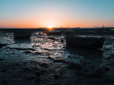Sahilde gelgit nedeniyle mahsur kalan bazı balıkçı tekneleri silüeti. Gün batımında, İspanya, Cadiz Körfezi bakan ıslak kum güneş ışığı yansıtır