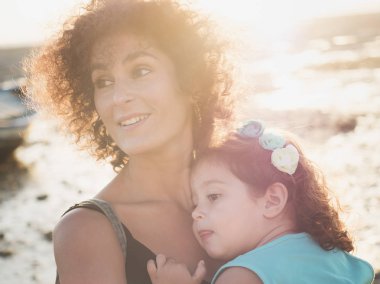 Küçük kız annesi sahilde günbatımı sırasında sarılma. Arka planda ıslak kum güneş ışığı yansıtan gelgit nedeniyle görebilirsiniz. Yumuşak stiliyle Vintage filtre