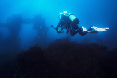 dalgıç batık doğru mavi deniz yoluyla bir dalış alarak onun kamera ile. Gemi eski kalıntıları uzak ve bulanık gizemli bir aura vererek bak