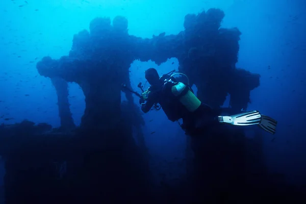 沈没船の残骸の写真を撮るダイバー 船の古い残骸は小さな魚がたくさんに囲まれ 青と濁った水を与える謎のオーラ — ストック写真