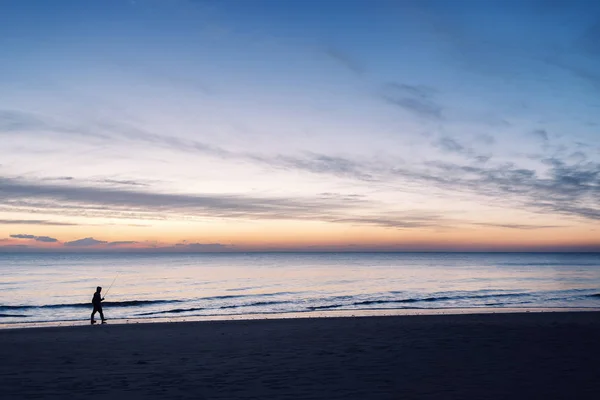 Pescador caminando por la orilla del mar al atardecer — Foto de Stock