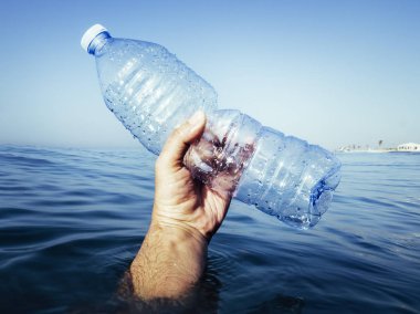 plastik bir şişe ile okyanustan çıkan el