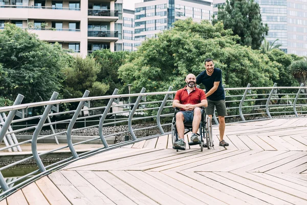 man in wheelchair walking at park with a friend
