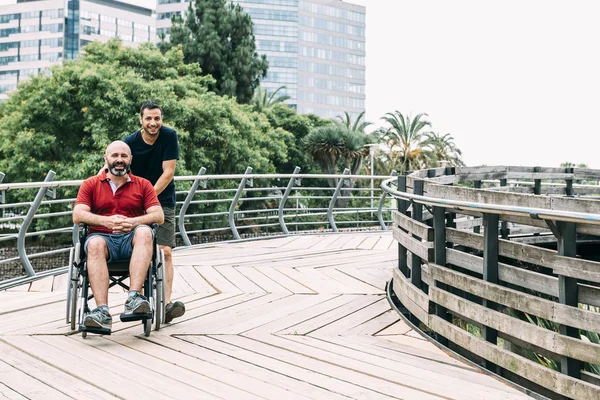 Man in wheelchair walks with a friend in the park — Stock Photo, Image