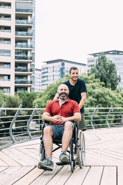 Man in wheelchair laughing with a friend at park — Stock Photo, Image