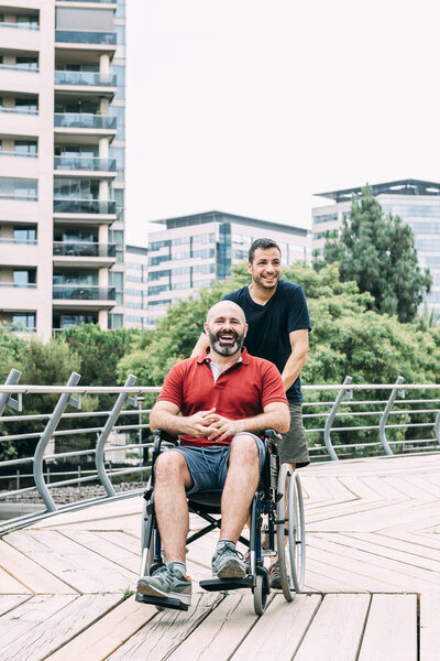 man in wheelchair laughing with a friend at park