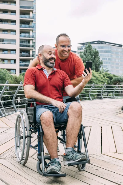 Man in wheelchair watching the phone with a friend — Stock Photo, Image