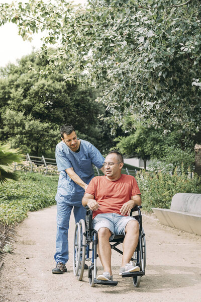 man in wheelchair talking with his nurse at park