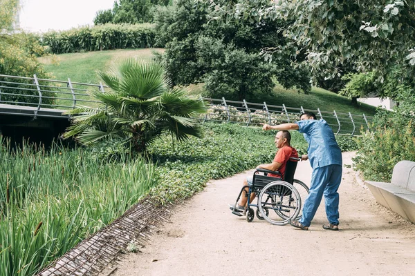 Man in a wheelchair talking with his caretaker — Stock Photo, Image