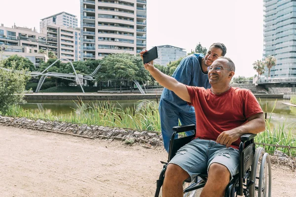 Man in wheelchair taking a photo with his nurse — Stock Photo, Image