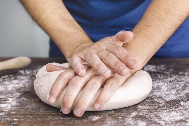 Ahşap bir masada ekmek hamuru yoğuran tanınmamış bir kadının elleri. Evde sağlıklı yiyecek kavramı.