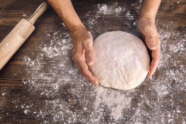 Tanınmayan birinin elleri un dolu bir ahşap masadan ekmek hamuru alıyor. Evde sağlıklı yiyecek kavramı.