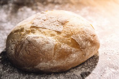 Sabah güneşi ile aydınlatılan taze pişmiş kır ekmeği un dolu ahşap bir masa üzerinde, evde sağlıklı yiyecek kavramı.
