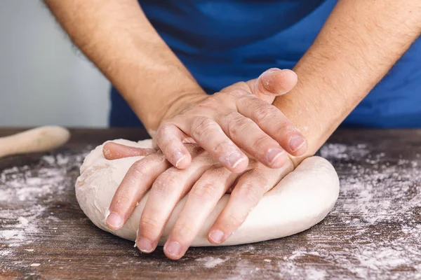 hands of an unrecognizable woman kneading bread dough on a wooden table, concept of healthy food at home