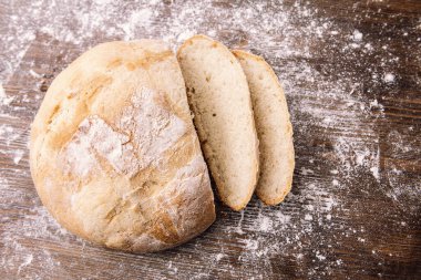 Un dolu ahşap bir masada kesilmiş bir somun rustik ekmeğin üst görüntüsü, evde sağlıklı yiyecek kavramı.