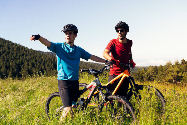two men pointing the route they are going to take with their mountain bike through the countryside, concept of sport and healthy lifestyle in nature
