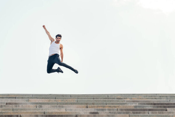 handsome sportsman jumping up at the top of a staircase celebrating success, concept of urban sport and healthy lifestyle, copy space for text