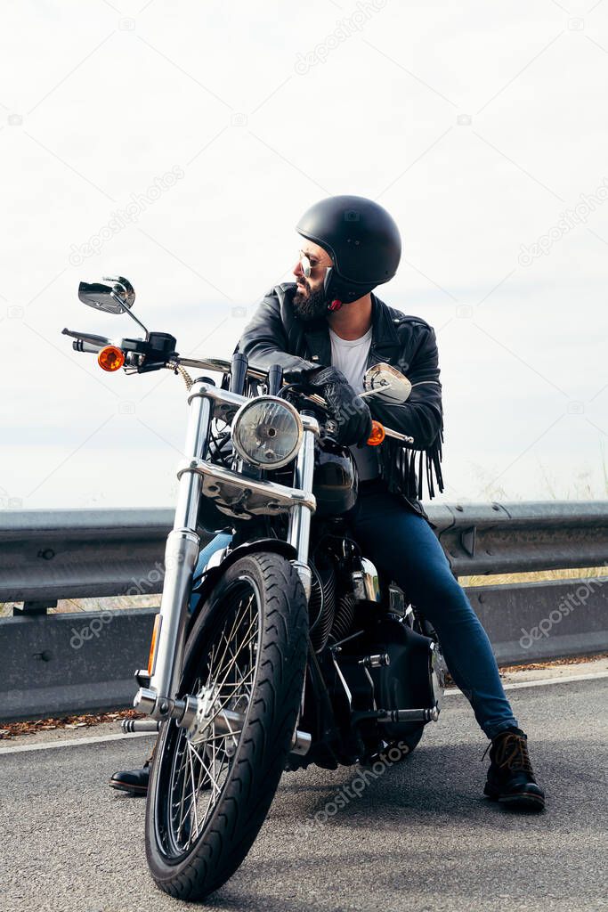 vertical photo of a biker with helmet and leather jacket sitting on his bike, concept of freedom and rebellious lifestyle, copy space for text