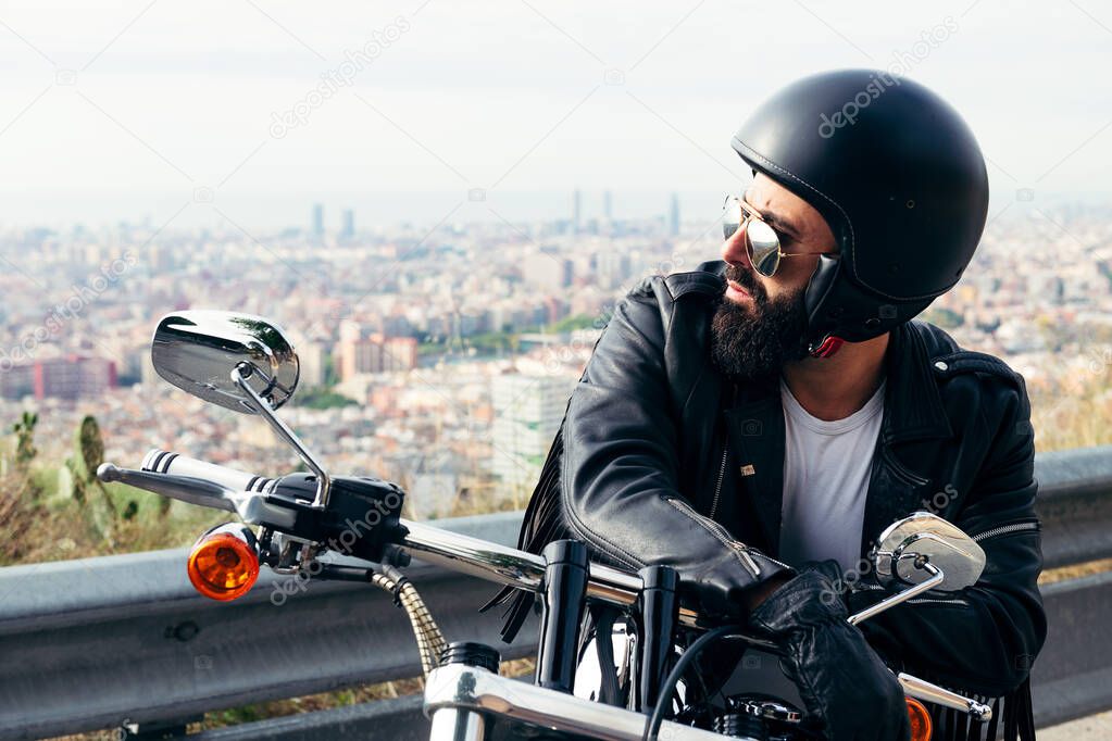 biker with helmet and leather jacket sitting on his motorcycle with the city in the background, concept of freedom and rebellious lifestyle, copy space for text
