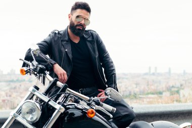 Deri giyen ve güneş gözlüğü takan bir adam motosikletinin yanında poz veriyor, özgürlük ve motorcu yaşam tarzı, metin için kopyalama alanı