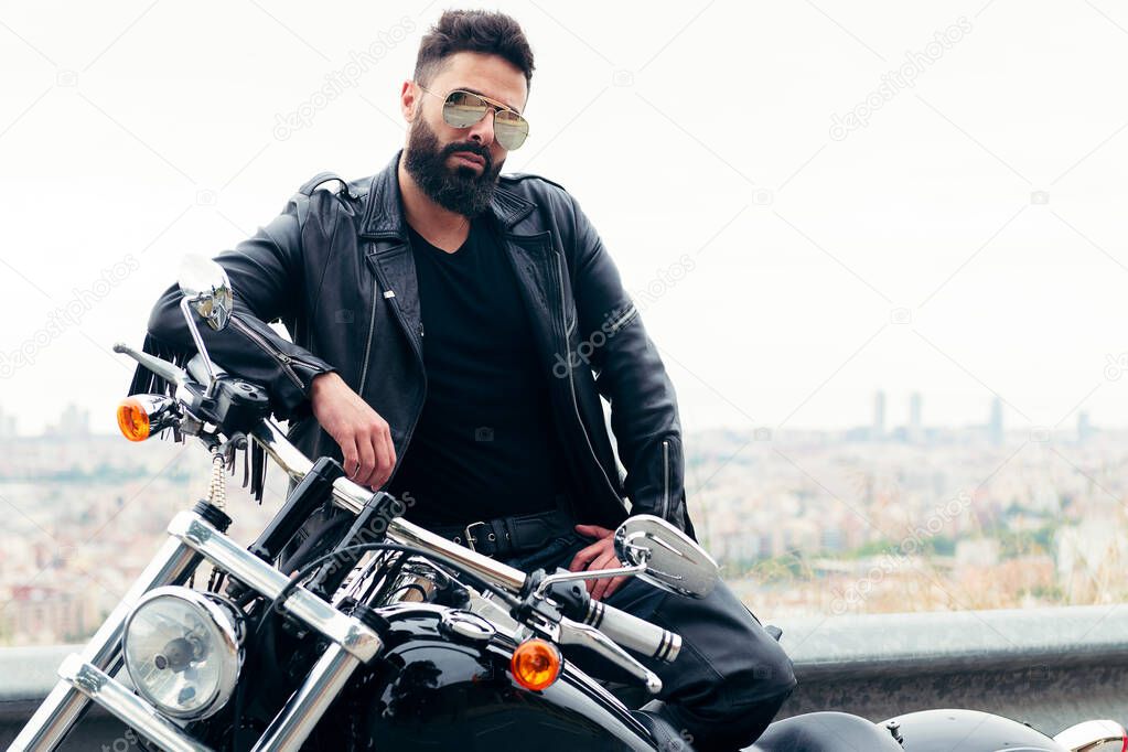 man dressed in leather and wearing sunglasses poses next to his motorcycle, concept of freedom and biker lifestyle, copy space for text