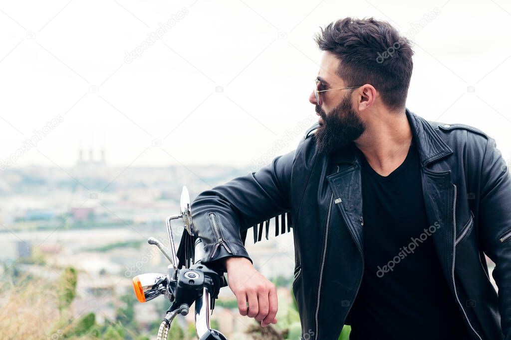 portrait of a bearded man in a leather jacket leaning against the handlebars of his motorcycle, concept of freedom and biker lifestyle, copy space for text