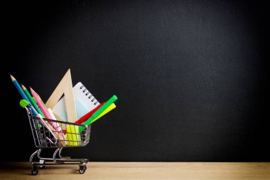 Okul tebeşir tahtasının arkasındaki ofis malzemeleri süpermarket arabasında duruyor.