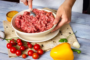 İnce ahşap bir masada pirzola pişirme işlemi. Kadın elleri baharat serpiyor ve kıyma yapılmış etin üzerine zeytin yağı döküyor. Pirzola yap