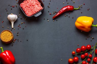 Koyu gölgeli mutfak çerçevesi arka planında kıyma, biber, baharat, kiraz domatesleri, paprika, hardal tohumu, sarımsak