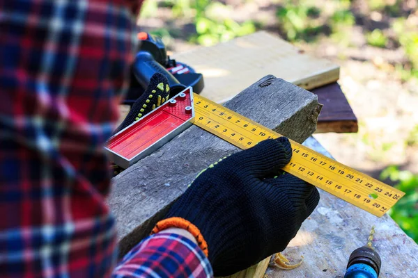 Adam ahşap bir tahtanın üzerinde inşaat meydanı ile ölçüm yapıyor.