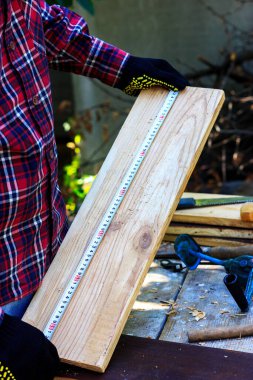 Tahtayı mezurayla ölçüyorum. Marangozluk atölyesi. İş eldivenli bir adam..