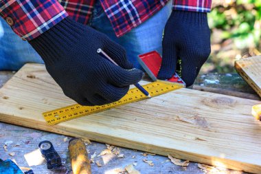 Adam ahşap tahtalarda inşaat cetveli çiziyor.