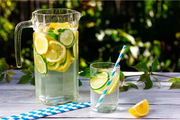 График прохладной воды с ломтиками лимона и лайма на светлом деревянном столе. — стоковое фото