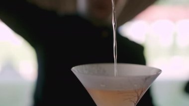 Siyah gömlekli adam yavaş çekimde kokteyl martini bardağına içki dolduruyor.