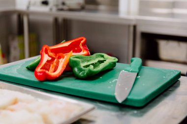 Mutfakta büyük bir bıçakla yeşil bir masanın üzerinde açık kırmızı ve yeşil biber.